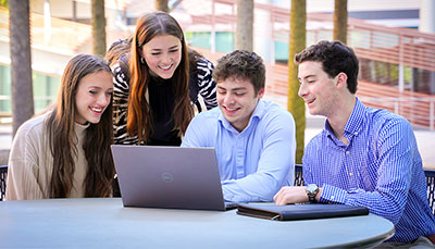 Group of students working together around a laptop at an outdoor table. 