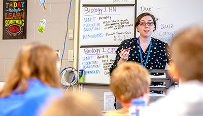 Teacher standing in front of a whiteboard engaging with students in their class. 