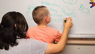 Teacher helping a student write on a whiteboard. 