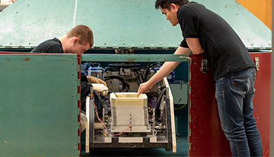 Two students working together at a large piece of equipment in an engineering lab.