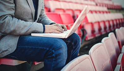 Person with a laptop on their lap sitting in bleacher stadium chairs. 