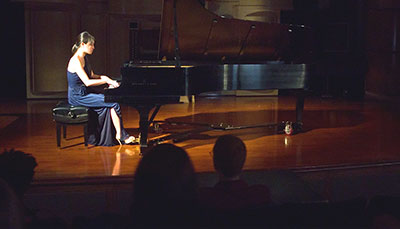 Performer on stage playing a baby grand piano. 