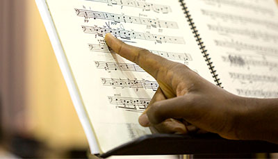 A close up of a music stand with sheet music and someone pointing to a note.