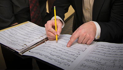 Someone making notes on pages of sheet music in a notebook.