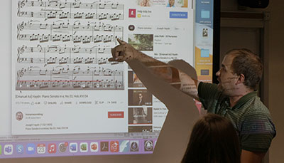 Music professor pointing to music on a projected smart board.