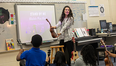 Music teacher standing in front of class with ukulele in hand