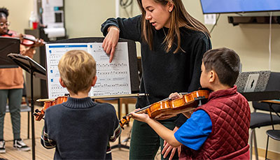 Student teacher working with young kids learning how to play the violin. 
