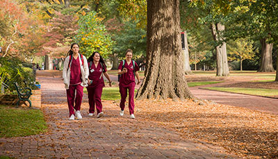 Three nursing students walking on brick walkway of Historic Horseshoe in fall.