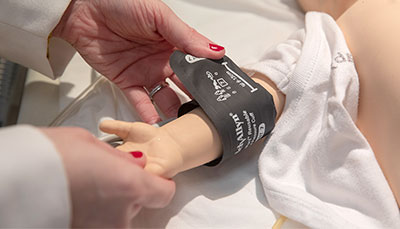 Nurse applying a blood pressure cuff to an infant healthcare simulation mannequin. 