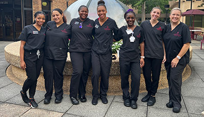 A group of nurses with scrubs outside the Nursing building on the Columbia campus.