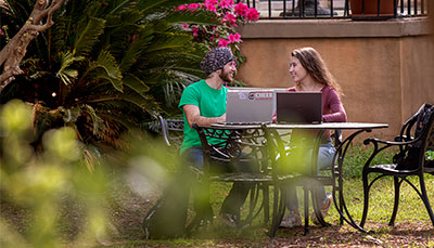 Two people sitting at an outdoor table with a laptop.