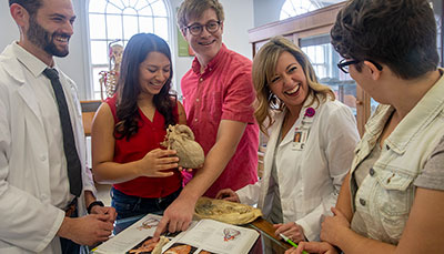 Medical students and a professor gathered to look at organ samples and compare them to the illustrations in a book.