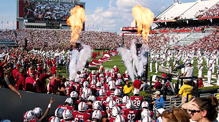 The football team running out onto the field before a game through clouds of smoke and fire in the air.