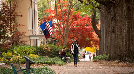Student walking down the brick sidewalk on a fall day beside the President's House.