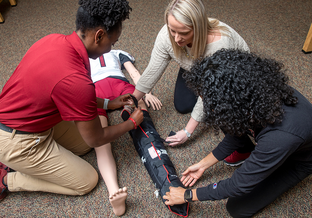 Student in an athletic training class, splinting a leg of a mannequin. 