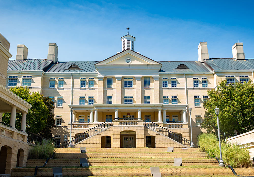 The Green Quad residence hall sits on a hill with its coupla and a weather vane standing out against a blue sky.