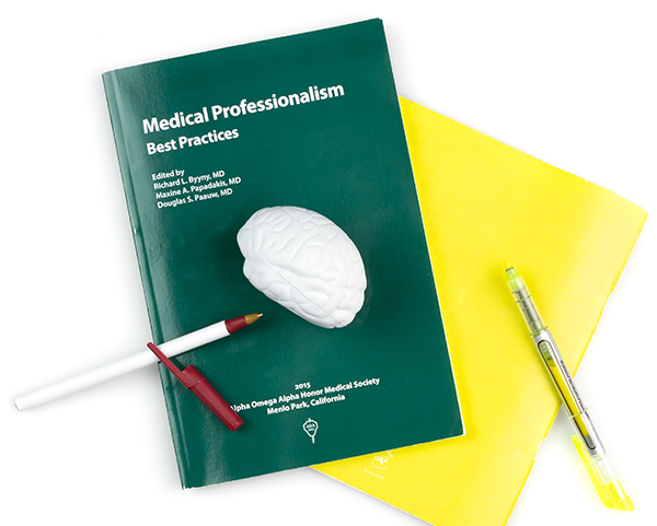 A book titled Medical Professionalism Best Practices with a notebook, pens and brain stress ball. 