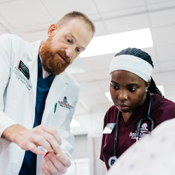 Clinician and nursing student work together at a patient’s bedside, demonstrating team-based neurological care and training.