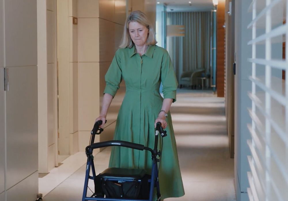 Woman walking down a hallway using a rollator walker, representing recovery and mobility support after neurological injury.