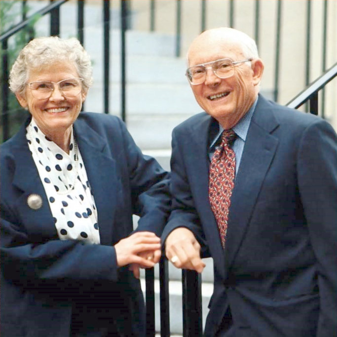 Mr. and Mrs. Vernberg stand in front of steps, both wearing navy suits.