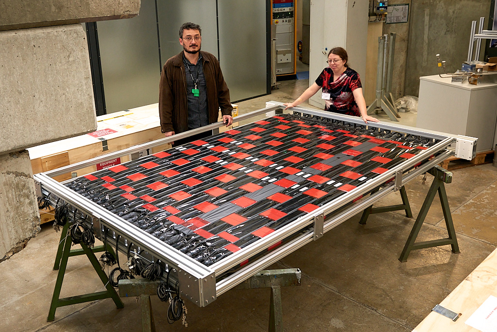 A scientist and a student stand behind an assembled detector, which resembles a checkerboard the size of a dining table.