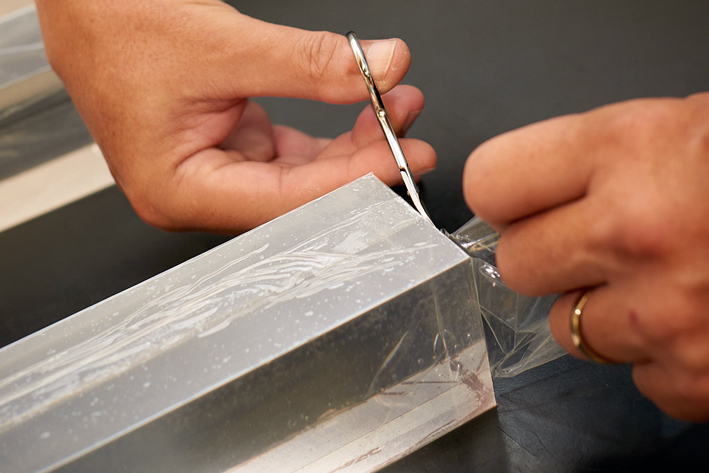 Ralf Gothe's hands are seen using scissors to trim the end of a long, clear bar that appears to be made of glass. 