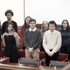 10 students stand behind a podium wearing business attire.