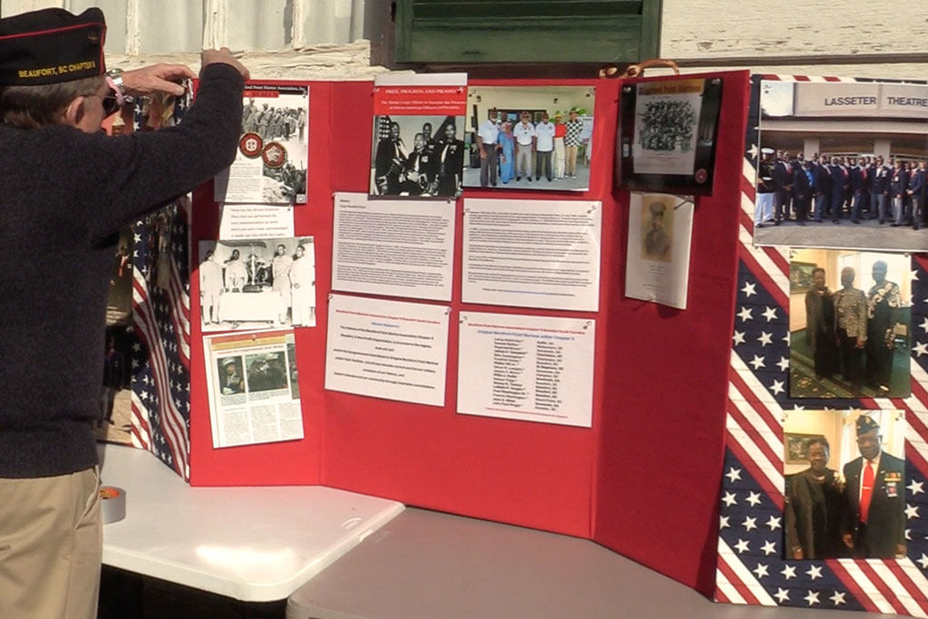 Photo of a veteran adding pictures to a poster display board outside of the Grand Army Hall of the Republic.
