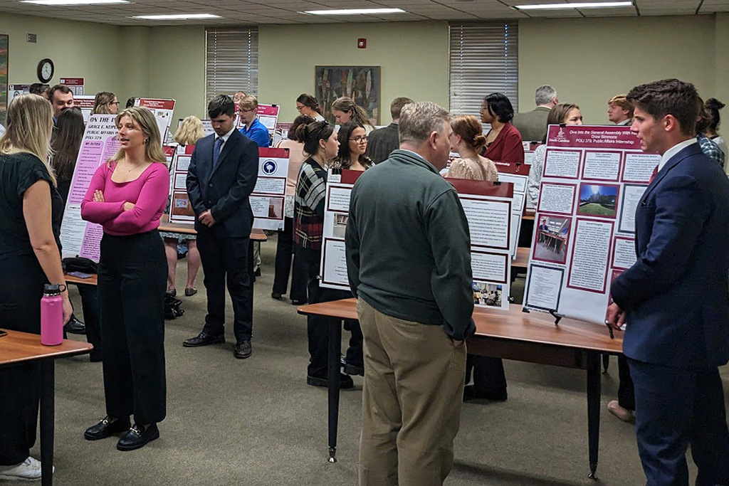 Students and professionals talk in groups standing beside posters the students presented for a mini career fair.