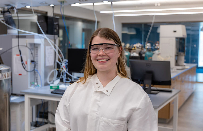 Kelly Forrester, wearing goggles and a white lab coat, smiles for the camera.