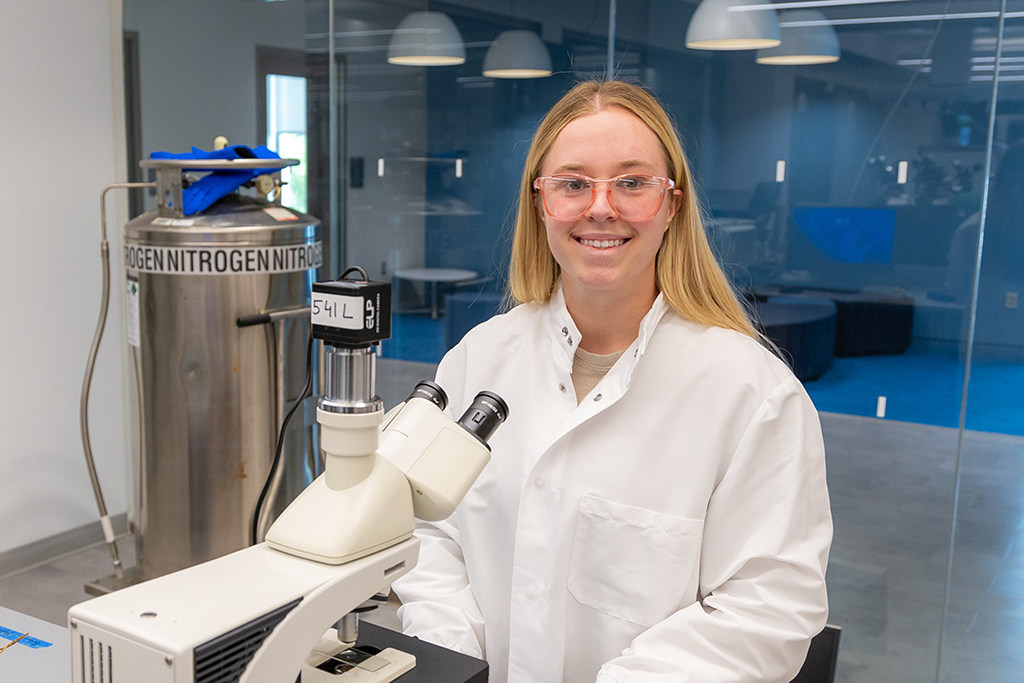 Katie McBride stands in front of a microscope in a laboratory setting.