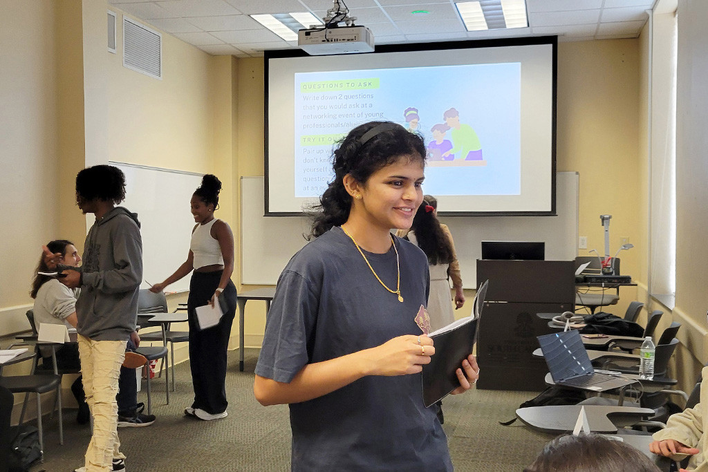 A student stands in front of her classmates with a book in hand.