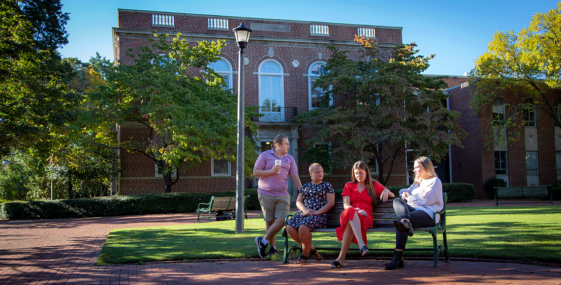 Students on a bench talking in front of Currell College.