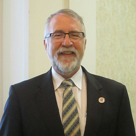 Paul Allen Miller, a gray haired caucasian male in a suit and tie, smiles.