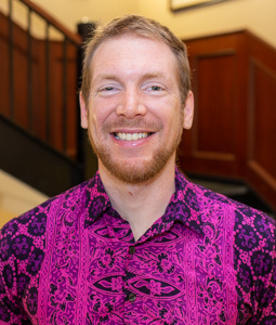Dan Frost has red hair, wears and pink and purple patterned shirt, and smiles at the camera.