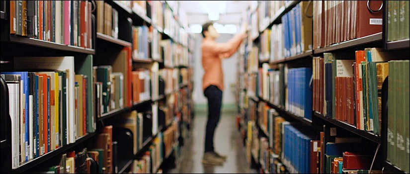 Student searching for book among shelves in library