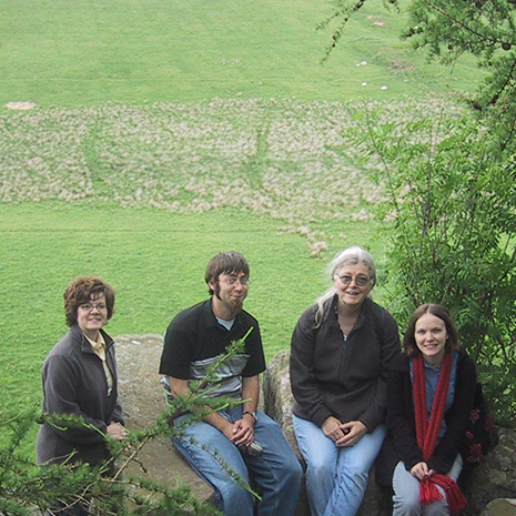 Professor Connie Schulz (center, right), and three students, pose in front of a vast field of green. They are on site at Hadrian's Wall.