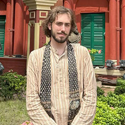 a man stands outside with a tan shirt on and scarf