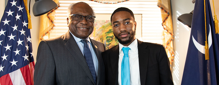 Jahleel Johnson and Congressman James Clyburn pose in a formal office setting. They are each wearing dark business suits with light colored button down shirts and ties.