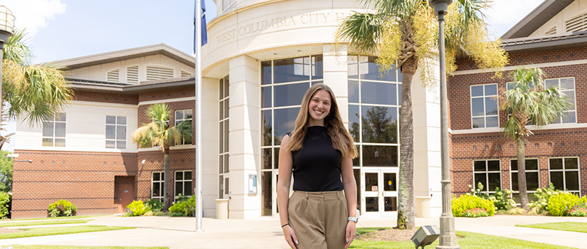 Claudia Case smiles in a headshot portrait taken inside a campus building. She has long light brown hair and is wearing a black sleeveless top.
