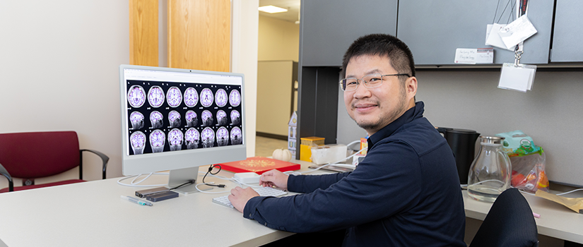 Feilong Ma sits at a computer displaying a series of brain scans.