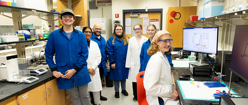 students and professors smiling in a chemistry lab