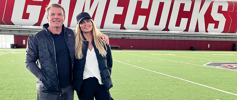 Justin Tupper stands with his wife on a football field with Gamecocks spelled out behind them.