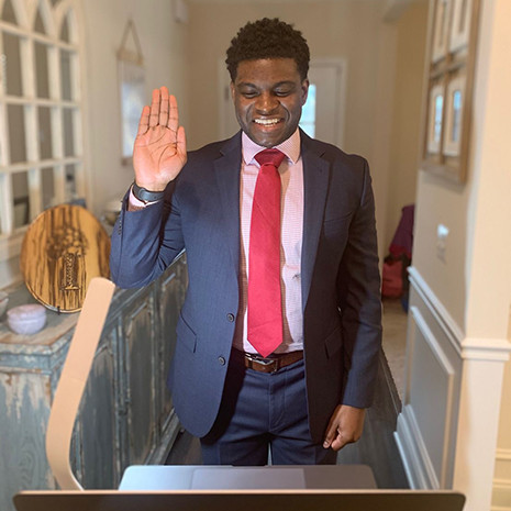 James Anderson raises his right hand while looking at a computer screen during a virtual swearing in ceremony