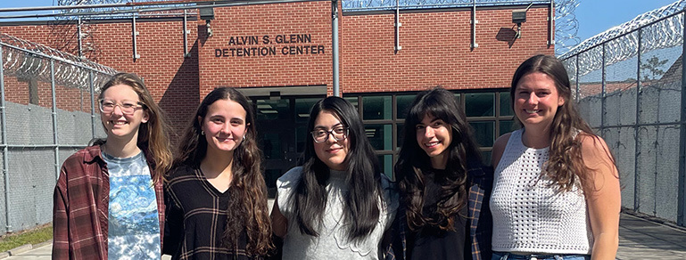Five women, including USC criminology Ph.D. student Christina Plakas, standing outside the Alvin S. Glenn Detention Center in front of its brick entrance and security fencing.
