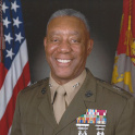 Wilson smiles at the camera in military uniform in front of official flags.