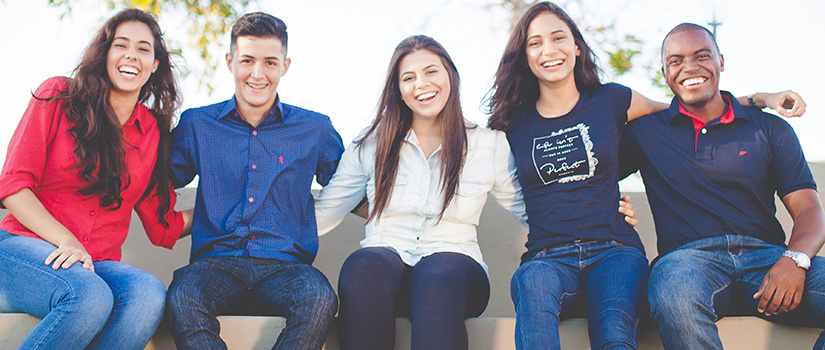 Five students sit, arms around each other, smiling at the camera.