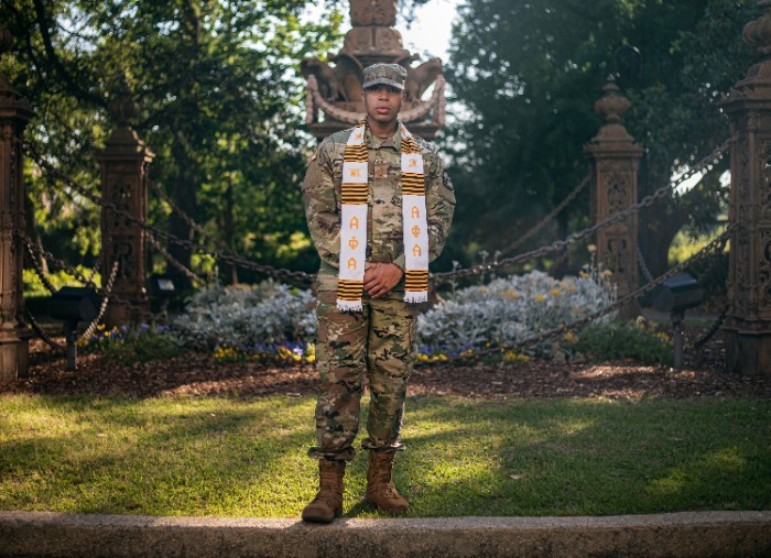 Dajuan McDonald stands on the Horseshoe wearing Army fatigues and a banner for Alpha Phi Alpha