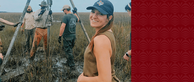 Sarah Hall stands in a marsh wearing a tank top and baseball cap