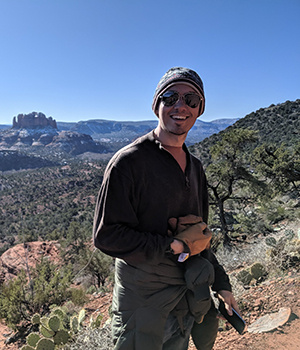 Keller VandeBogert poses in front of scenic view with blue sky and landforms behind.